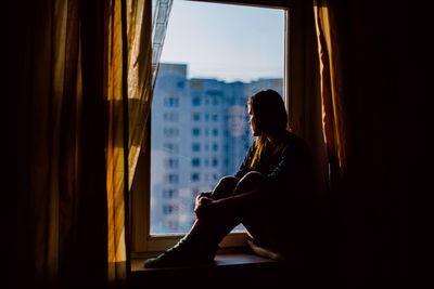 Thoughtful woman sitting on window at home