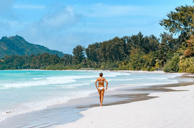 Woman in white bikini walking on sandy beach.