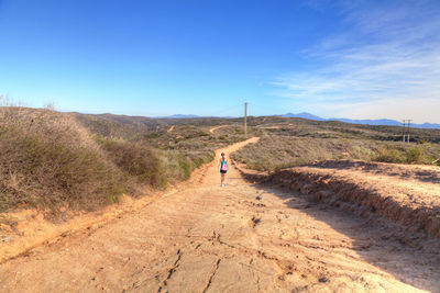 Rear view of person walking on desert against clear blue sky