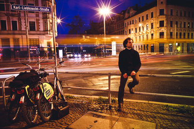 Full length of man sitting on railing at night