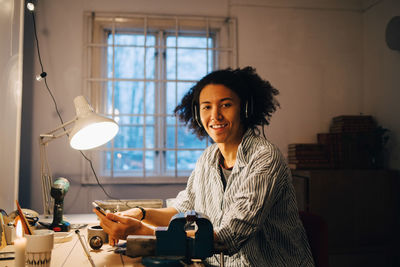 Portrait of smiling technician working on equipment while listening music at desk in workshop