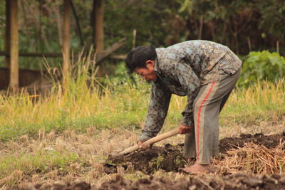 Side view of man standing by tree trunk