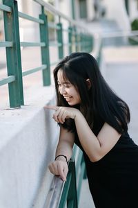 Smiling young woman standing by railing outdoors