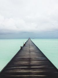 Wooden pier amidst sea against cloudy sky