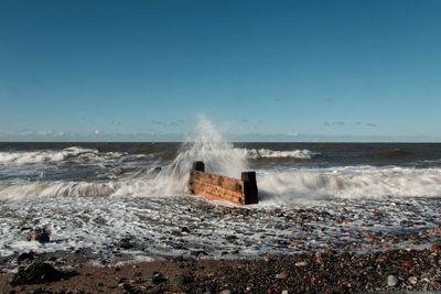 Waves splashing on shore against clear sky