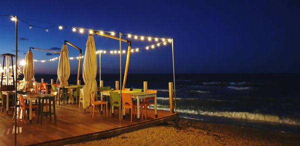 Illuminated restaurant at beach against clear sky at night