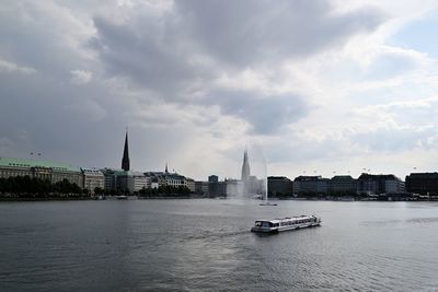 View of city at waterfront against cloudy sky