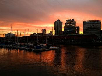 Boats moored at harbor against buildings in city during sunset