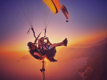 Low angle view of people paragliding against sky during sunset