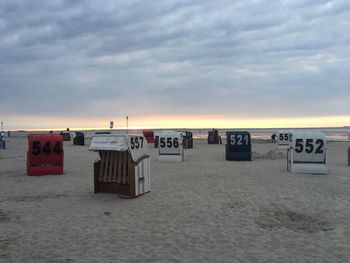 Hooded chairs on beach against sky during sunset