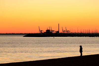 Silhouette person standing by sea against sky during sunset