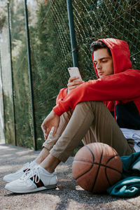 Trendy young man with mobile phone and outdoor basketball