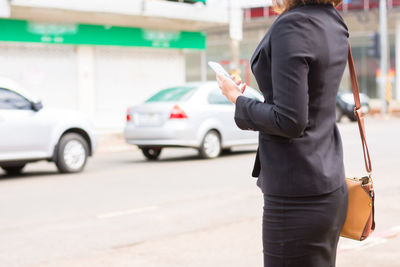 Man holding mobile phone while standing on car in city