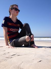 Young man wearing sunglasses on beach against clear sky