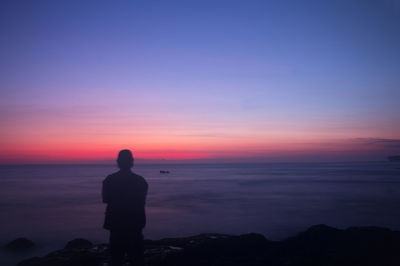 Silhouette man looking at sea against sky during sunset