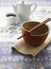 Close-up of bowl and chopsticks with teapot on table