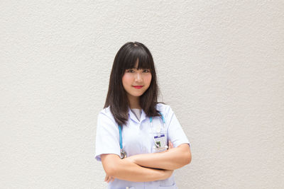 Young female doctor standing against wall