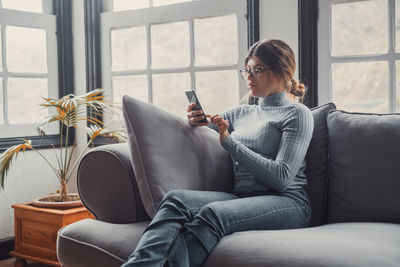 Young woman using phone while sitting on sofa at home