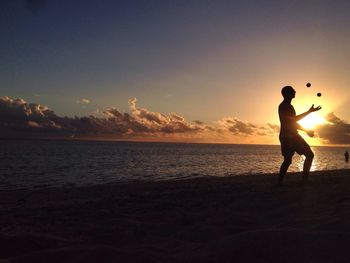 Silhouette of woman standing on beach at sunset