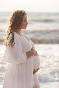 Beautiful pregnant woman wear white dress posing over sea at background closeup. healthy lifestyle