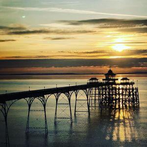 Silhouette railing by sea against sky during sunset