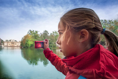 Portrait of woman with mobile phone by lake against sky