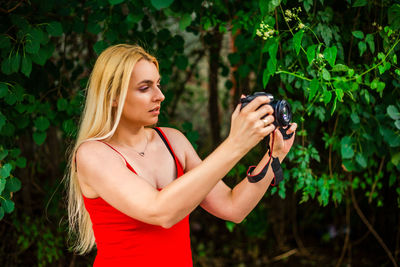 Young woman using mobile phone while standing against plants