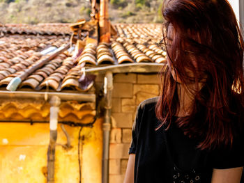 Close-up of young woman with tousled hair standing by house