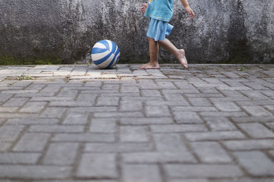 Low section of child playing with ball on footpath