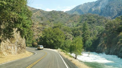 Road amidst trees and mountains against sky