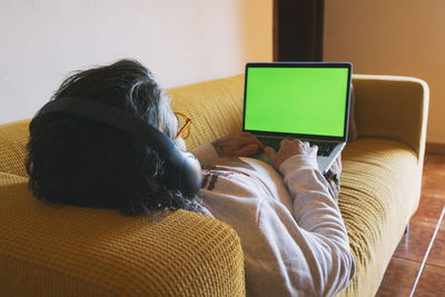 Relaxed man sitting on sofa at home looking at laptop person