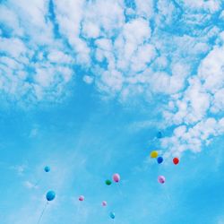 Low angle view of balloons flying against blue sky