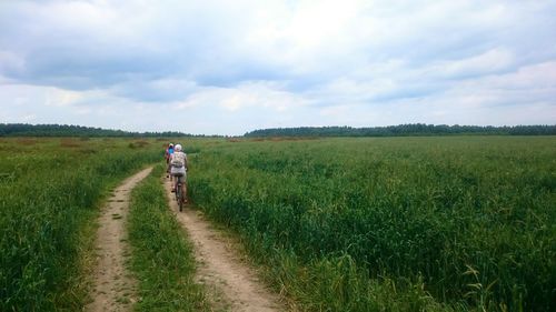 Dirt road on grassy field against cloudy sky