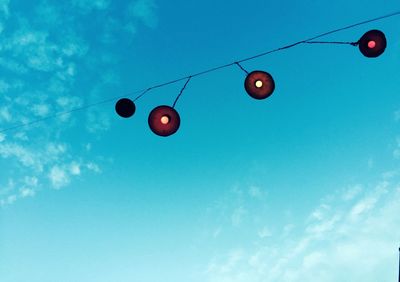 Low angle view of illuminated lighting equipment hanging on cable against sky