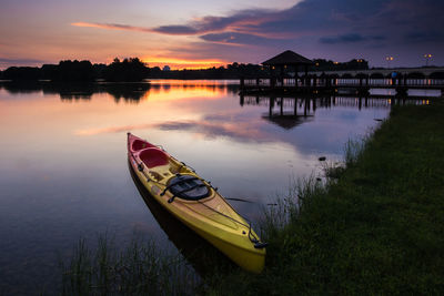 Boat moored on lake against sky during sunset