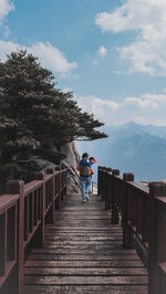 Rear view of woman walking on footbridge against sky