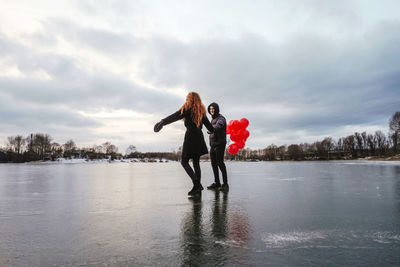 Woman standing by lake against sky during winter