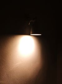 Low angle view of illuminated light bulb against wall