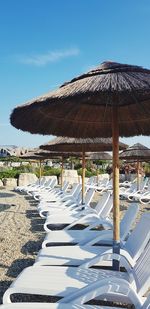 Lounge chairs and parasols on beach against blue sky