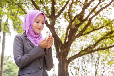 Smiling young woman praying while sitting in park