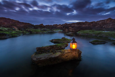 Scenic view of rocks by lake against sky at dusk