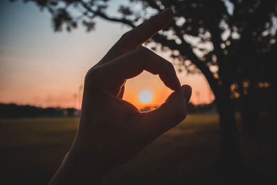 Close-up of silhouette hand holding sun during sunset