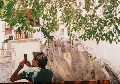 Rear view of man photographing against trees