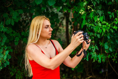 Young woman using mobile phone while standing against trees