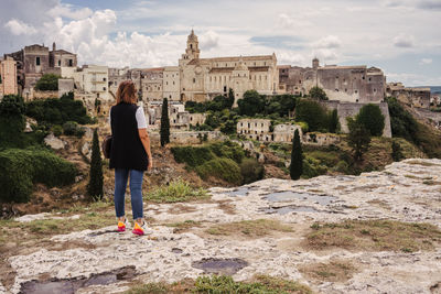 Rear view of woman standing by buildings against sky