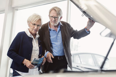 Senior couple examining car engine in showroom