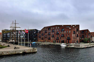 Sailboats in river by buildings against sky