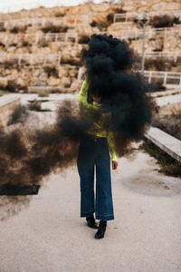 Contemporary unrecognizable lady in trendy wear among black smoke with city on background