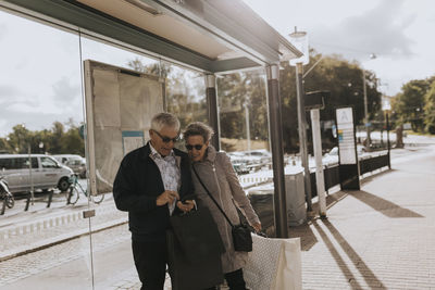 Senior couple checking phone at bus stop