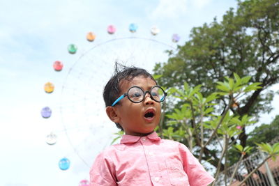 Low angle view of shocked boy standing against ferris wheel